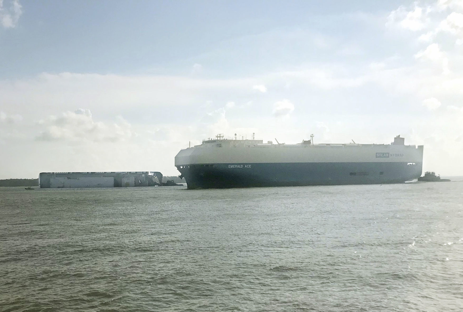 Carrier ship passes tipped freighter, departing from the port